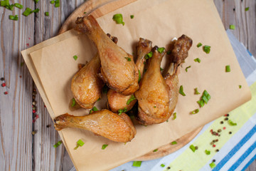 baked in the oven chicken legs with a green onion on a wooden board on a light wooden background