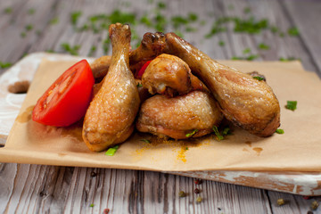 baked in the oven chicken legs with green onions and tomatoes on a wooden board on a light wooden background