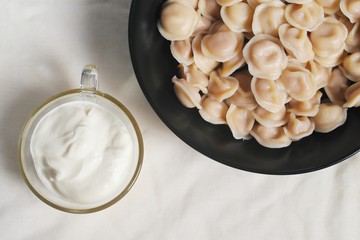 Traditional dish of dumplings in a bowl on a white tablecloth. Served with sour cream, a fork and a spoon.