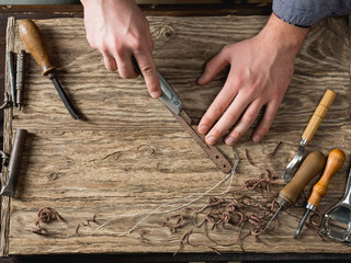Leather crafting instruments and master hands in workshop with tools and accessories on brown dark background. Flat top view, overhead. Big size resolution photo.