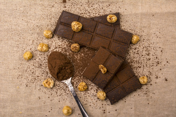 Bitter chocolate bar, nuts and spoon of cocoa on burlap fabric