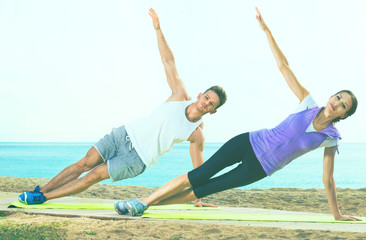 Young couple training yoga poses sitting on beach