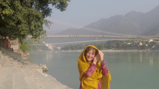 ]Woman pilgrim, caucasion, walks the banks of the Ganges River in Rishikesh, front side view, looking thoughtful. Smooth tracking shot, four times slow motion.