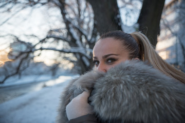 shy young woman looking over her fur coat on winter day 