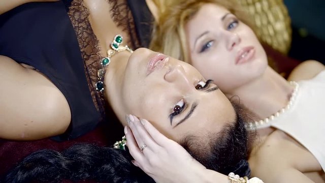 portrait of two young women with bright make-up, the lady posing in expensive jewelry lying on their backs