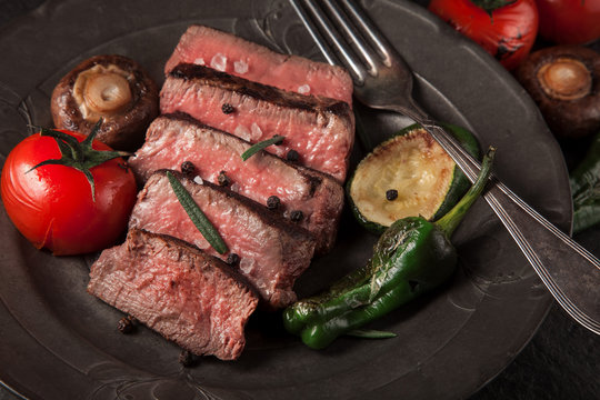 freshly prepared beef sirloin on a dark vintage plate background and grilled vegetables