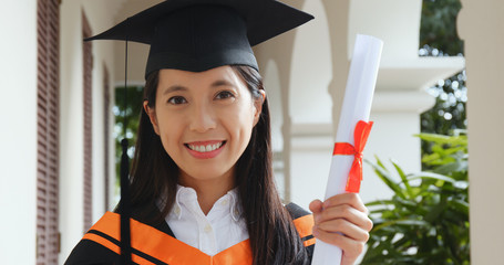 Excited woman wearing graduation gown in university campus