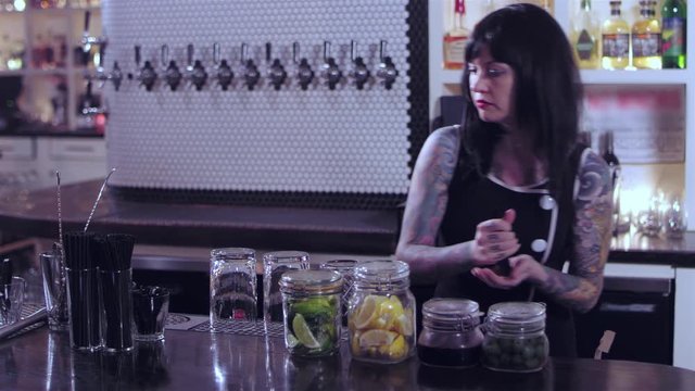 Attractive tattooed bartender lady organizing her ingredients, and drink preparation tools at a bar