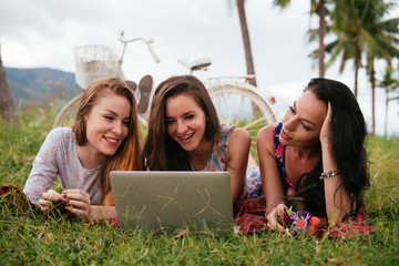 Women lay on grass using laptop together during picnic in the countryside