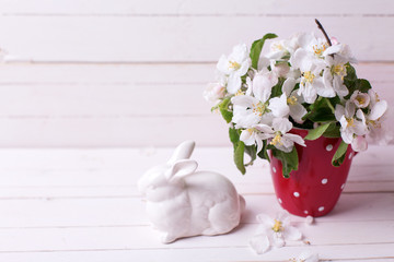 Apple tree flowers in  red cup and  Easter bunny on white wooden background.