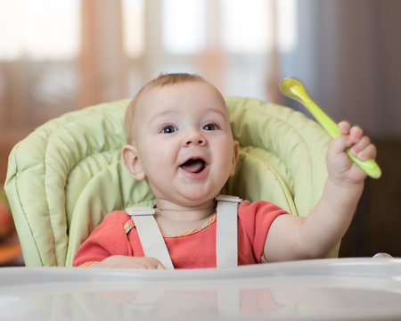 Happy Baby In High Chair With Spoon In His Hand