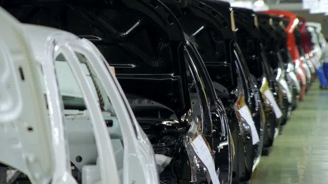 line of different colors car bodies are standing in an assembly shop in automobile factory