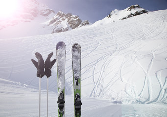 Skiing and ski poles stand vertically in the snow against the background of the ski descent