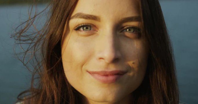 Close up of the attractive young woman looking on the side at the lake background and than looking to the camera. Portrait. Outdoors