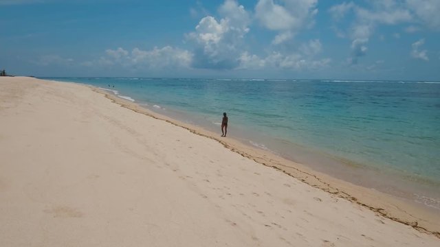Young girl in a swimsuit walking on the beach. Aerial view of on tropical beach Bali,Indonesia. Travel concept, Aerial footage, 4K video.