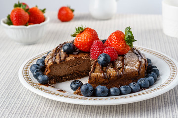 Big chocolate cheesecake with blueberry strawberry raspberry on a round plate.
