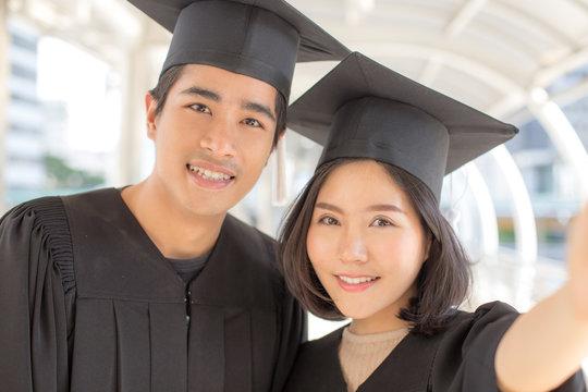 Young Asian People Students wearing Graduation hat and gown, city background, People with Graduation Concept. Woman Holding Smartphone for Selfie.