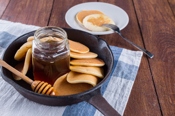  pancakes in a cast-iron frying pan on wooden table and honey