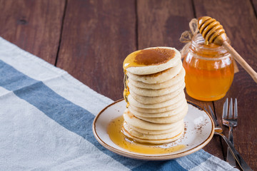 high stack of pancakes with honey on a white plate and a wooden background