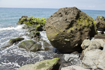 Beach Ponta de Sol rocky green coastline with cliffs and big volcano stones, Madeira island, Portugal
