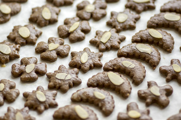 Brown moravian dark gingerbreads with sliced almonds on white baking paper one by one, christmas cookies, Variety of shapes