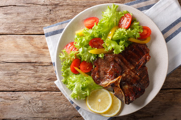 Delicious grilled T-bone steak with fresh vegetable and lemon close-up. horizontal top view
