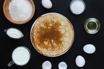 Russian pancakes with ingredients for cooking on black background