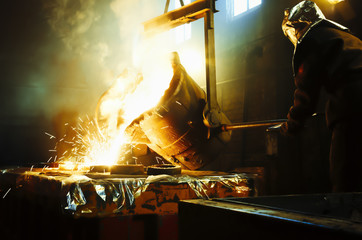 Worker controlling metal melting in furnaces. Man operates at the metallurgical plant. The liquid metal is poured into molds. - Powered by Adobe