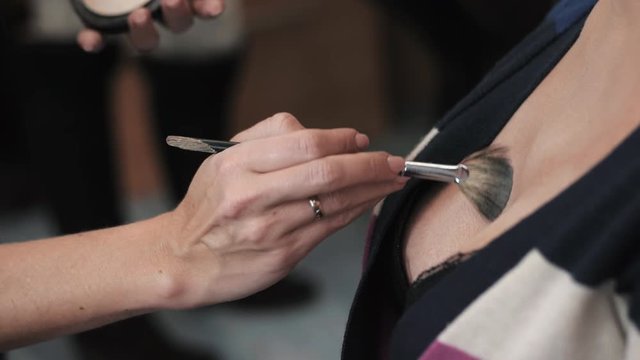 Professional makeup artist applying powder on model's decollete area. Beauty salon. Slow motion.