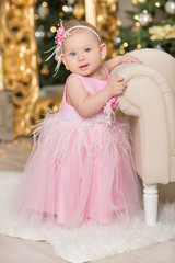 Christmas Happy funny baby child enjoying studio decorations New Year in pink dress on casual chair sofa close to xmas tree