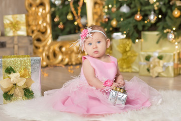 Obraz na płótnie Canvas Christmas Happy funny baby child enjoying studio decorations New Year in pink dress on casual chair sofa close to xmas tree