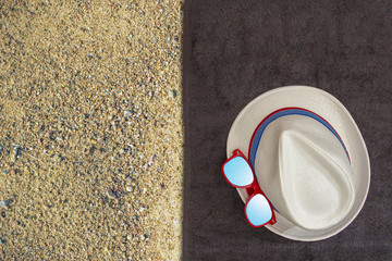 Male set of things for summer holidays (hat, sunglasses) on a on a dark towel and yellow sand background. Top view.