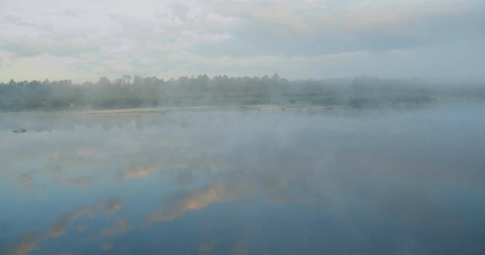 Flying low over the calm river. Dense fog over the water. The sun rises from behind the trees. calm water. Trees reflected in the water. the morning mist spreads over the river