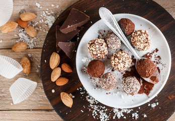 Prepare assorted dark chocolate truffles with cocoa powder, coconut and chopped almonds closeup. Homemade candy. Selective focus