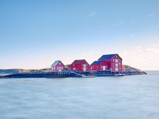Norway fishing village on stony island. Shinning red white houses in quiet bay. Smooth water level mirroring