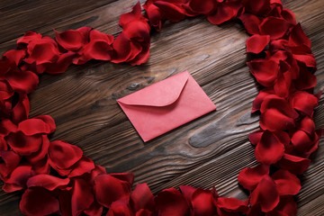Valentine day heart wreath with red rose petals and envelope top view on wooden background. Love letter concept