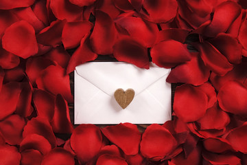 White envelope in red rose petals with golden wooden heart top view. Valentines day, romantic, love letter concept