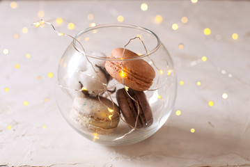 French tasty macaroon cookies in glass bowl with lights and cotton flower close up