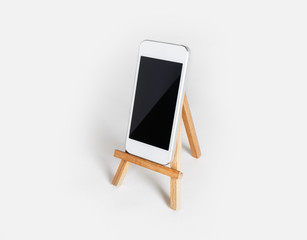 Smartphone with blank screen on wooden stand at white paper background. Mockup for placing your design.