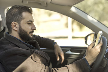 Bearded man in his car looking smartphone after parking while waiting