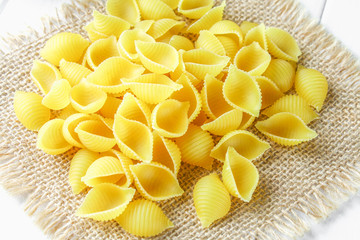 Culinary background with conchiglie pasta on wooden table. Pasta in the form of seashells on a sack with parsley.