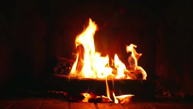 Orange flames from burning logs in indor open fireplace in super slow motion.