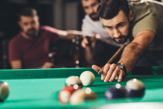 young handsome man playing in pool with friends at bar