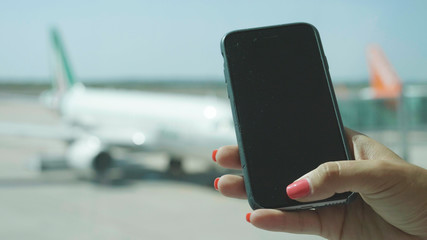 Beautiful young girl at the airport, looking at her phone before catching the flight