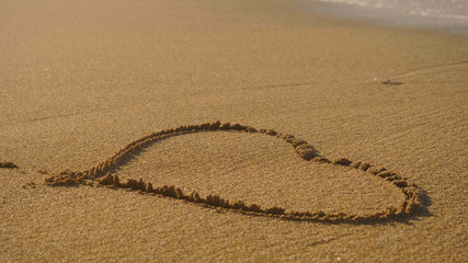Painted hart on brown sand, washed off by wave, sunset, sea background. Concept: rest, love, style life, sea, beach, coast.