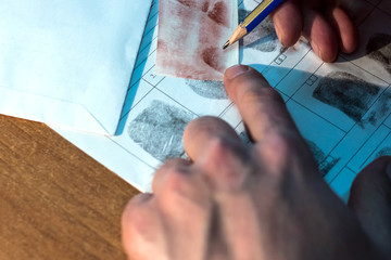 The forensic reader compares fingerprints. Close-up of male hands with a pencil.