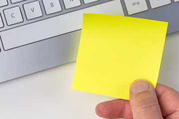 Human hand holding yellow sticky note