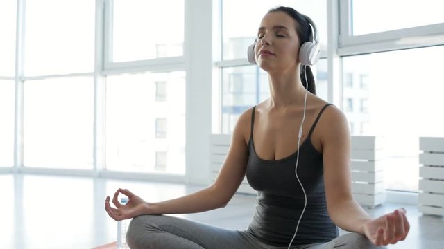 Pleased atmosphere. Close up of relaxed young woman using earphones while sitting on the floor and doing yoga