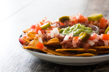 Mexican nachos with beef, guacamole, cheese sauce, peppers, tomato and onion in plate on wooden table