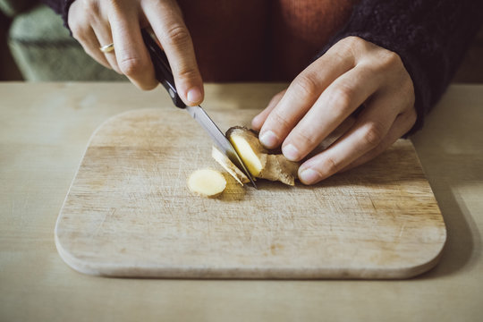 Woman's hands cutting ginger on wooden board, close-up